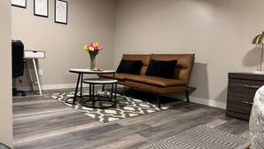 A modern living room with a brown leather sofa, a small round table, a vase with flowers, and a patterned rug. - Cozy&Private Basement Suite. Minutes from Airport, Highway, College, Restaurants (Thunder Bay)