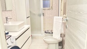 Ein kleines Badezimmer mit Dusche, Toilette, Waschbecken und einer Waschmaschine.