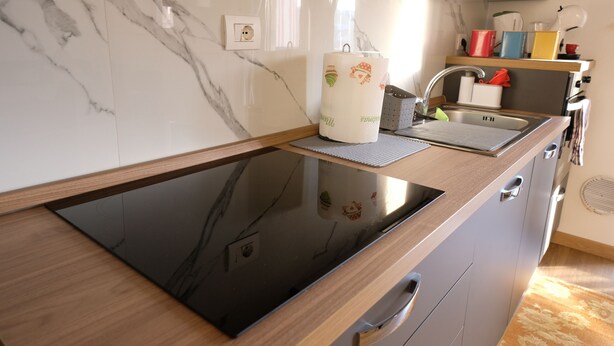 Eine moderne Küche mit einem schwarzen Induktionskochfeld, einer Holz Arbeitsplatte, einer Marmor-Spritzschutzwand und einem Edelstahl-Spülbecken.
