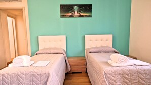 Ein Hotelzimmer mit zwei Betten, jeweils mit gesteppter Bettdecke und Kissen, sowie einem Wandbild über den Betten.