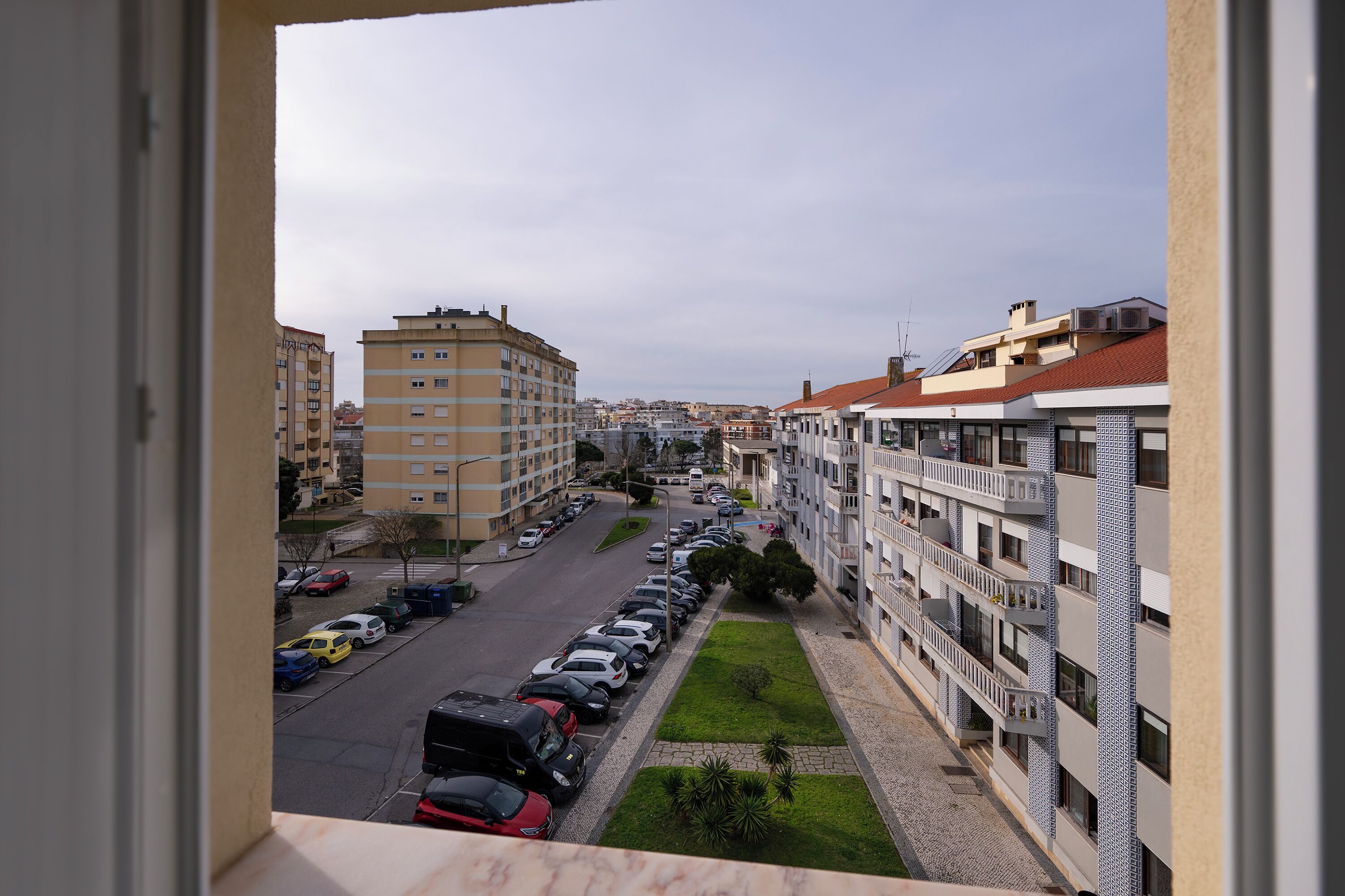 A view of a multi-story residential building with balconies, a parking lot with cars, and a green lawn area.