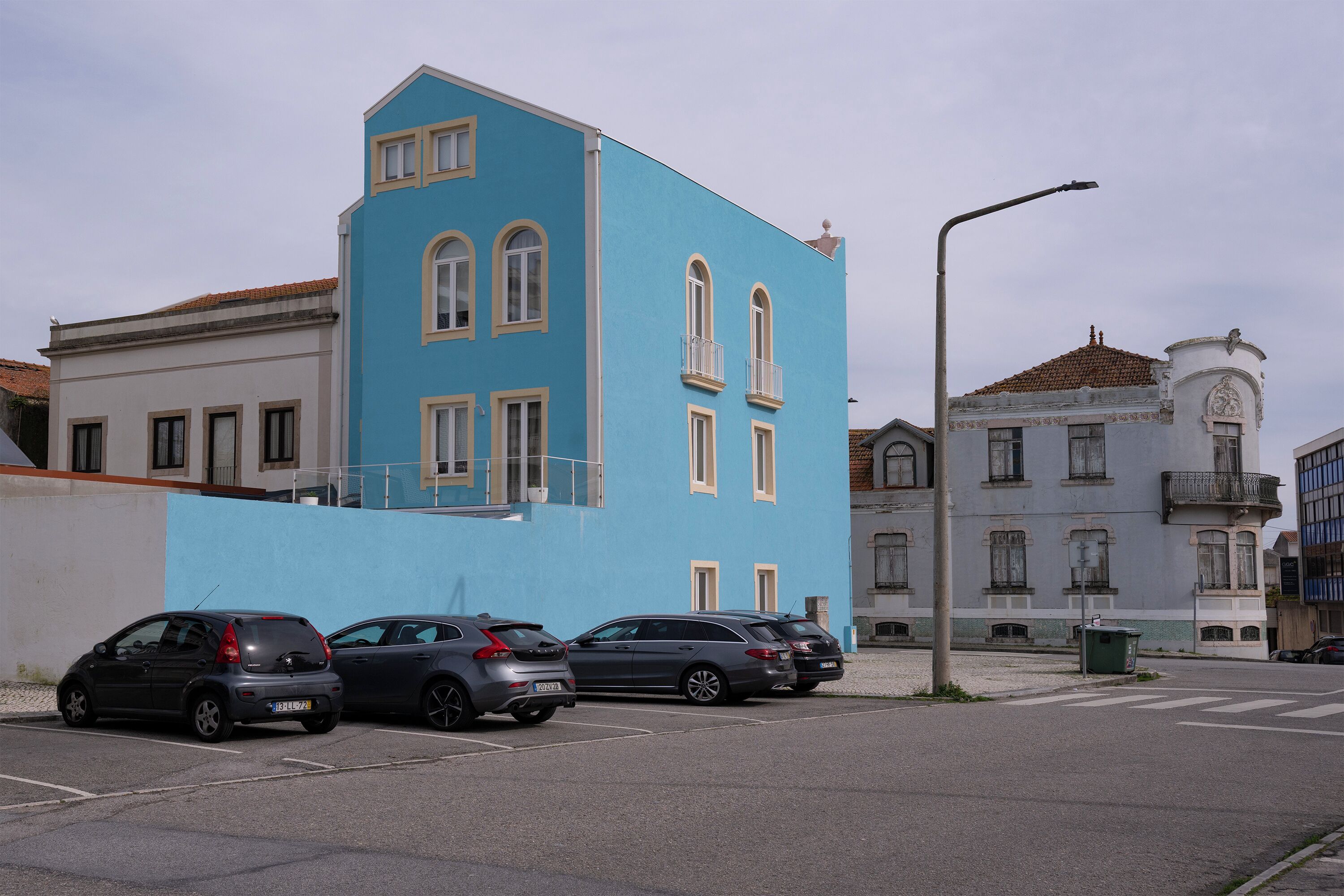 A parking lot with three cars parked in front of a blue building with white trim and arched windows.