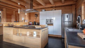 A modern kitchen with wooden beams, a central island, stainless steel appliances, and a black countertop. - Chalet Uska - Enjoy the thrill of the Alps all year round - OVO Network (Combloux)