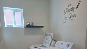 Een wasserette met twee voorladers, een raam, een plank met toiletartikelen, en een bord waarop staat 'The Laundry Room'.