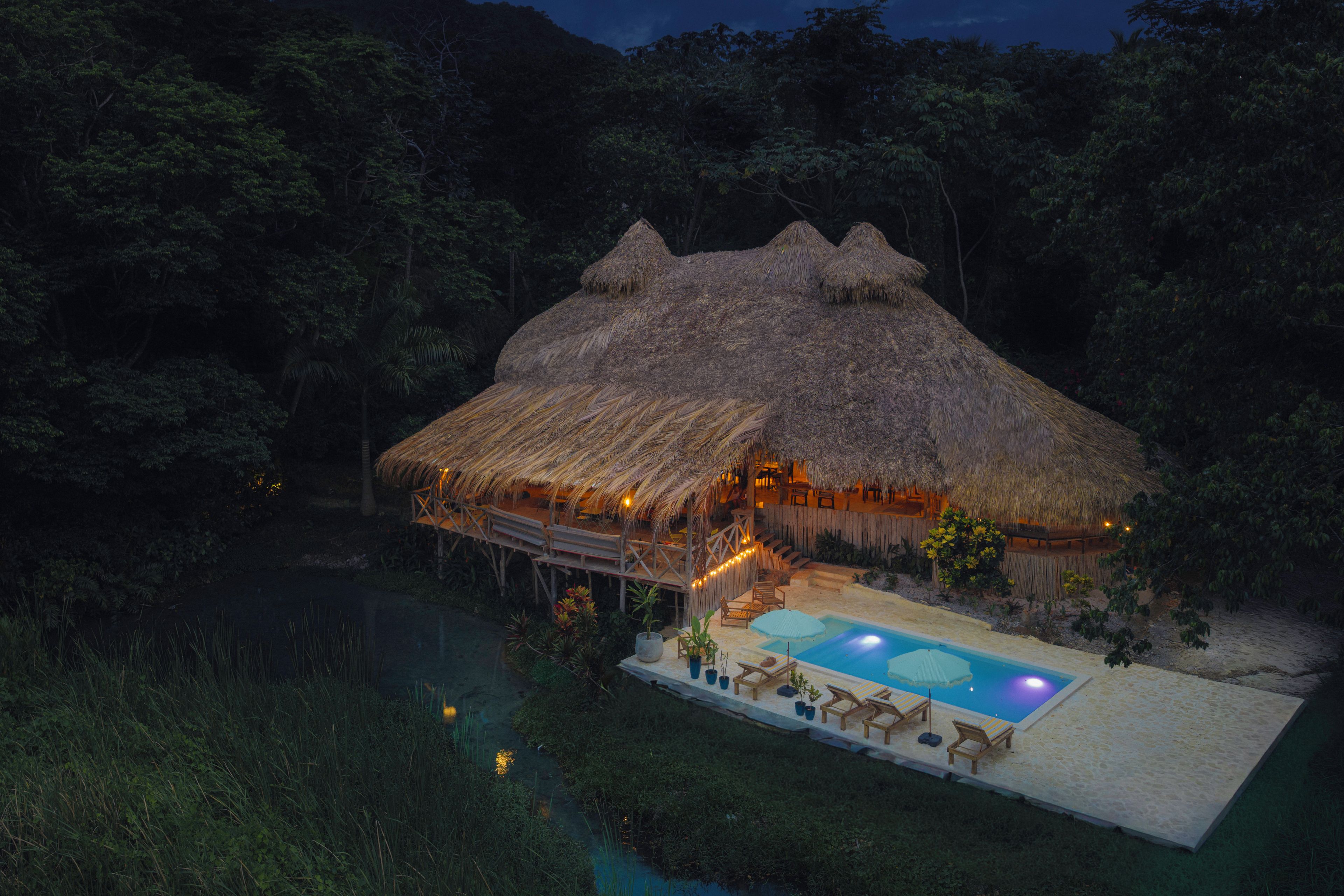 A thatched-roof structure with a pool and lounge chairs.