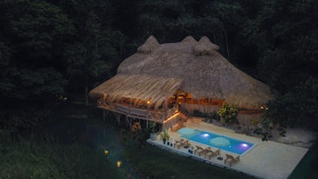A thatched-roof structure with a pool and lounge chairs.