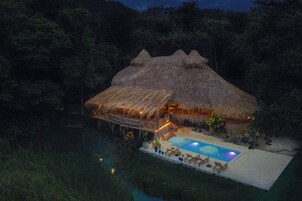 A thatched-roof structure with a pool and lounge chairs.
