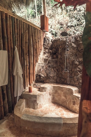 Zona de baño de piedra con pared de madera y valla de bambú.