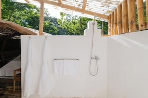 A white shower enclosure with a handheld showerhead, a towel rack with two towels, and a wooden pergola structure.