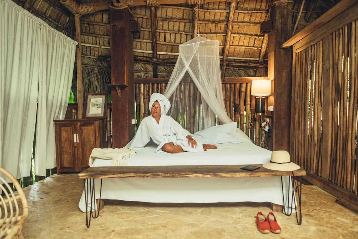 A room with a bed, a wooden table, a chair, a lamp, and a mosquito net.