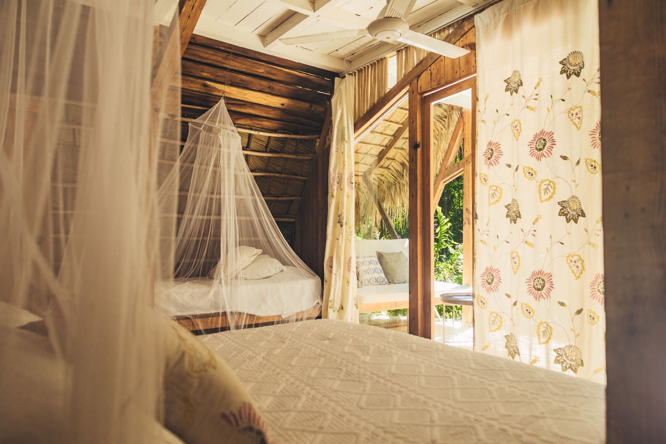 A bedroom with a canopy bed, wooden ceiling beams, and a view of greenery outside.