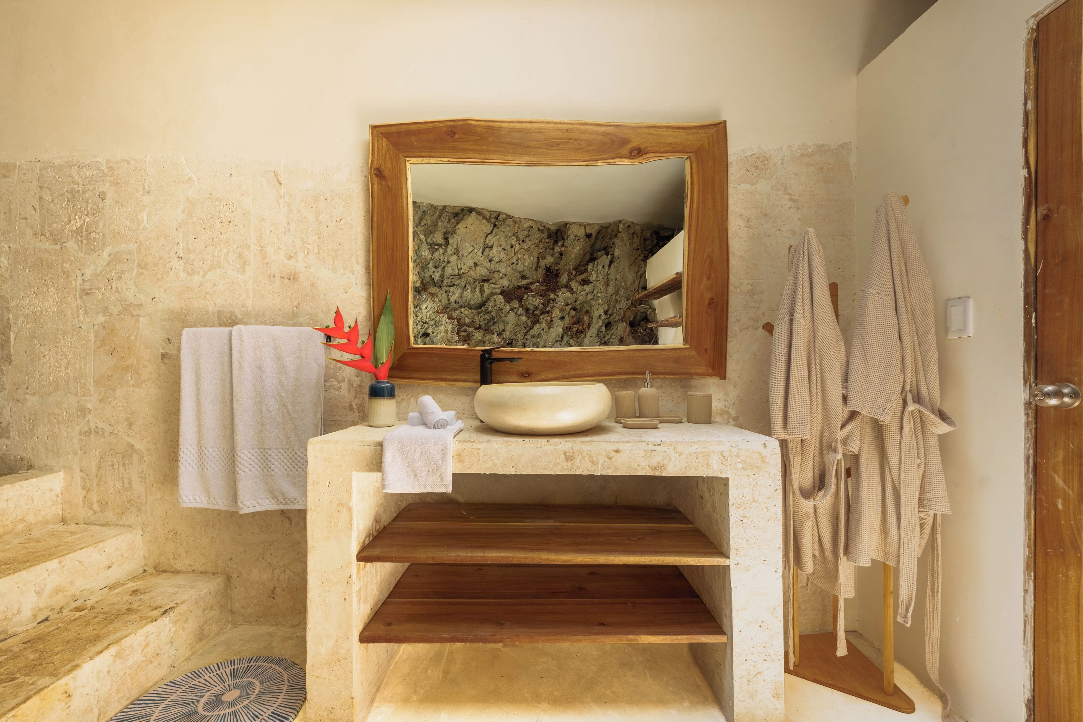 Une salle de bain avec un mur en pierre, un meuble-lavabo en bois, un évier, un miroir, une serviette et un peignoir.