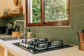 A kitchen with a gas stove, a sink, and a window with a view of greenery.