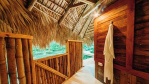 Interior de madera con techo de paja, baranda de madera y vista a la vegetación.