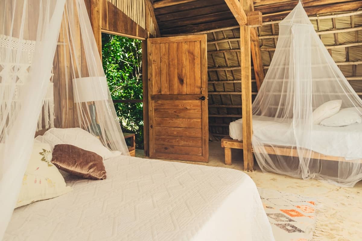 A rustic wooden room with a bed, a bench, and a door leading outside.