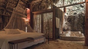 Una habitación con cama, un banco, una bañera de piedra y vistas a un paisaje rocoso.