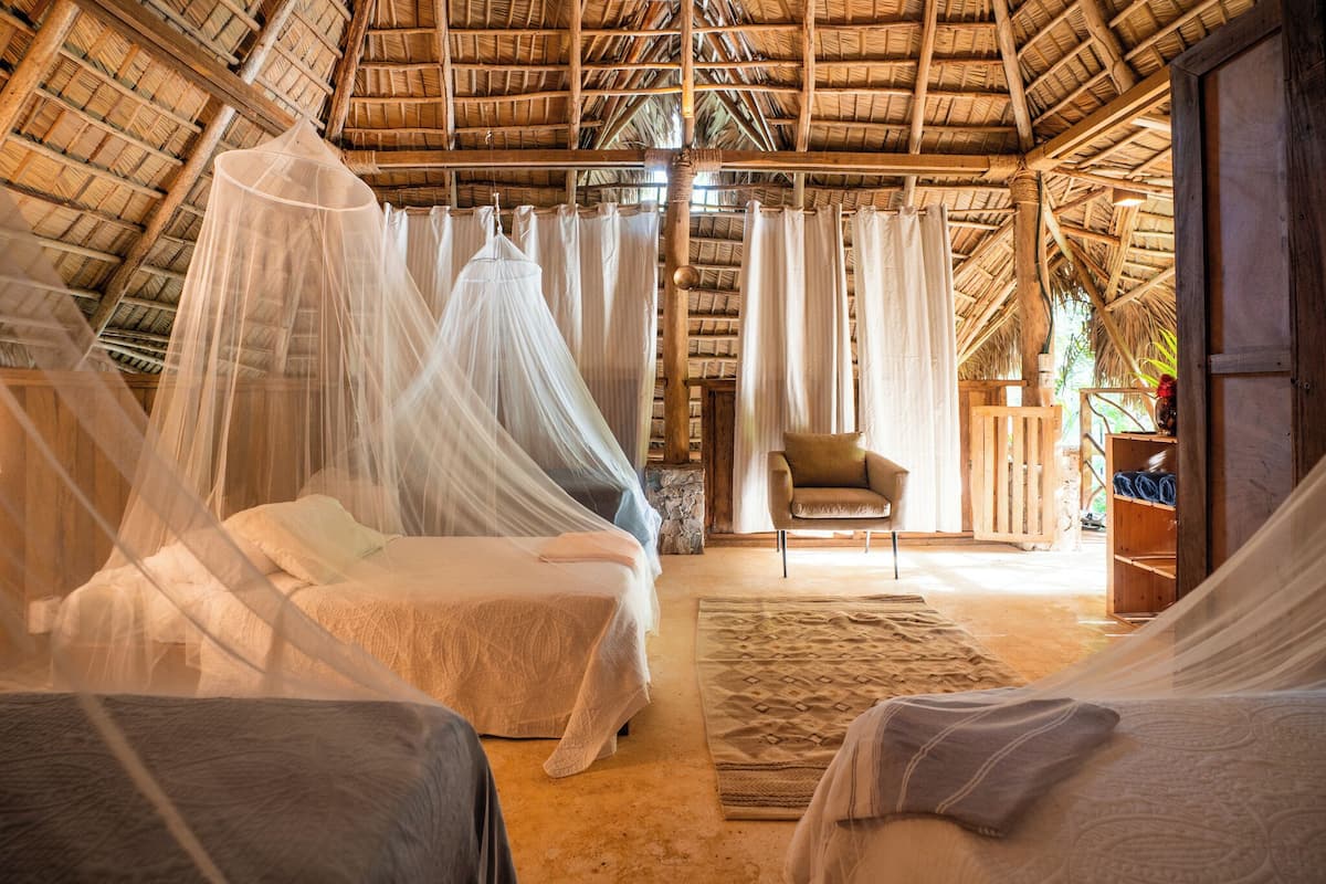 A room with two beds, a chair, and a thatched roof.