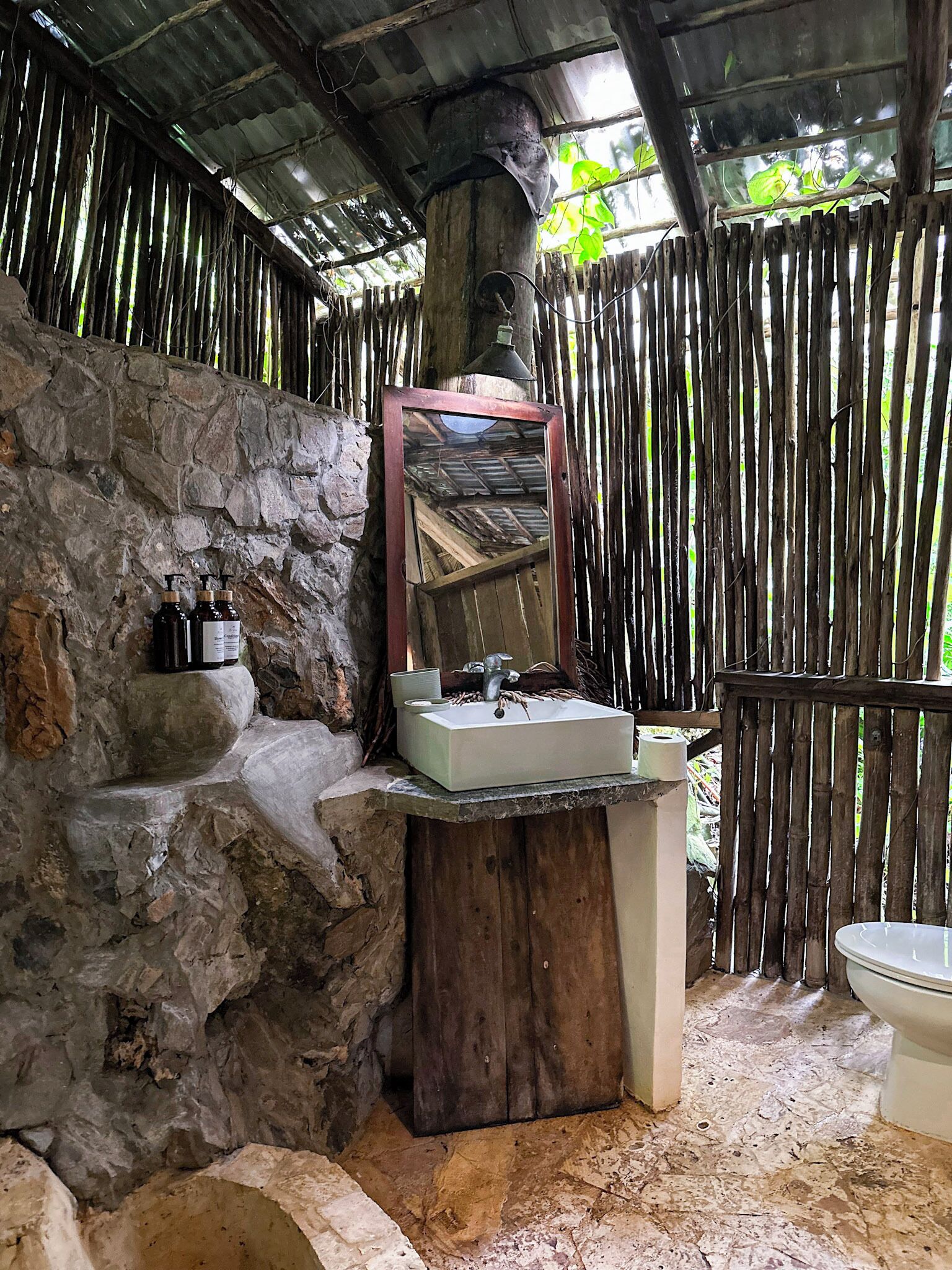 A rustic bathroom with a stone wall, a wooden sink, and a mirror.