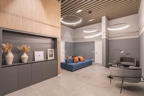 Ein moderner Empfangsbereich mit einem blauen Sofa, grauen Sesseln und einem Holztresen.
