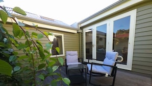 En inglasad uteplats med ett bord och två stolar, en skjutdörr i glas och utsikt över huset.