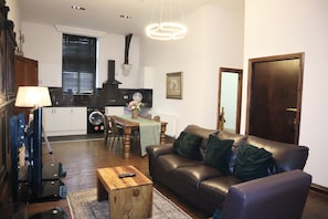 A modern living room with a leather sofa, wooden coffee table, and a dining area with a table and chairs. - Luxury Converted Church (Droylsden)