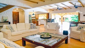 Uma sala de estar ampla com teto alto, sofás brancos, uma mesa de centro e vista para a cozinha e área externa.
