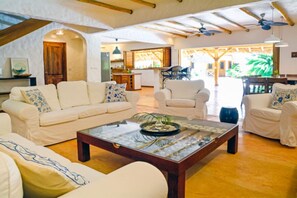 A spacious living room with a high ceiling, white sofas, a central coffee table, and a view of the kitchen and outdoor area. - Luxury Villa 50m from Playa Coson (Las Terrenas)