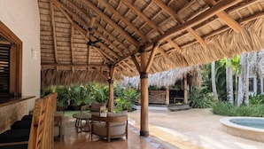 Um pátio externo com telhado de palha, móveis de madeira e uma piscina.