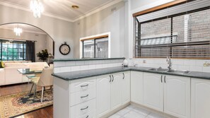 A modern kitchen with white cabinetry, a granite countertop, and a window with blinds.