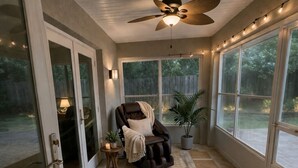 Ein Wintergarten mit Deckenventilator, Ledersessel, gemustertem Teppich und Blumentöpfen.