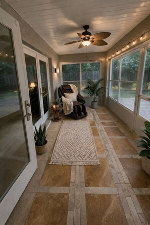 A sunroom with a ceiling fan, a leather chair, a patterned rug, and potted plants. - Cornerstone Hilltop Retreat (Inverness)