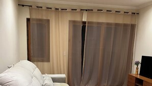 Un salon avec un grand canapé, un meuble de rangement en bois et une grande fenêtre avec des rideaux.