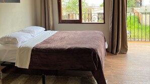 Une chambre à coucher avec un lit, une fenêtre avec des rideaux, une vue sur la verdure et un plafond en bois.