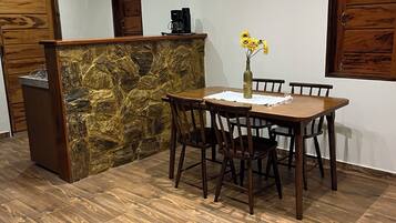A dining area with a stone accent wall, wooden table and chairs, a coffee machine, and a vase with flowers.
