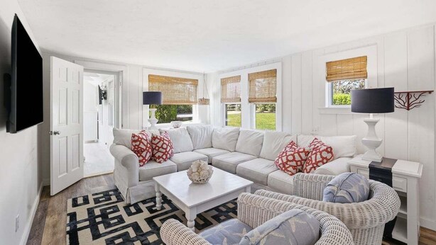 Un salon avec un canapé blanc, des fauteuils en osier, une table basse et un téléviseur fixé au mur.