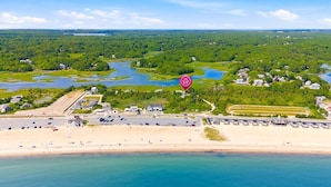 Vue aérienne d’une zone côtière comprenant une plage, un port de plaisance et une forêt dense.
