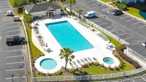 Vista aérea de un hotel con una piscina rectangular rodeada de sillones de descanso y una piscina circular más pequeña.