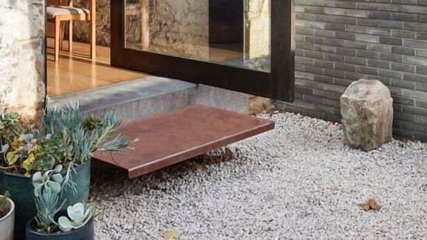 Une maison moderne avec une façade en pierre, une grande porte vitrée et un petit patio agrémenté de plantes.