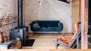 Une pièce chaleureuse avec une cheminée noire, un canapé vert foncé et un fauteuil en cuir.