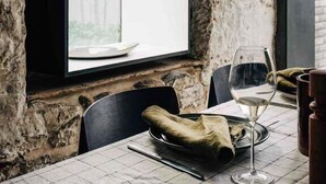 Un coin repas agrémenté d’un mur en pierre rustique, d’une grande fenêtre et d’une table mise avec un verre à vin, une assiette et une serviette.