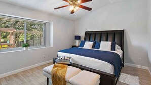 Ein Schlafzimmer mit Bett, einer Bank, einem Deckenventilator, einem Fenster und Blick ins Freie.
