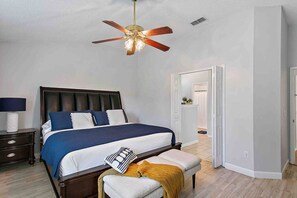Ein Schlafzimmer mit Bett, Nachttisch, Bank und Deckenventilator.