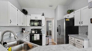 Eine moderne Küche mit weißen Schränken, einer Edelstahl-Spüle, einer Mikrowelle, einem Backofen und einem Kühlschrank.