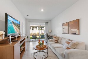 Ein modernes Wohnzimmer mit Flachbildfernseher, einer Couch, einem Couchtisch mit Dekoration und Blick auf die Terrassenanlage.
