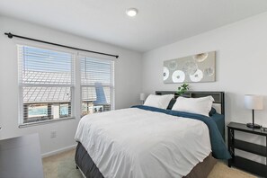 Ein Schlafzimmer mit einem Bett, einem Nachttisch, einer Lampe und einem Fenster mit Jalousien.