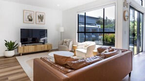 Una sala de estar moderna con un sofá de cuero, un televisor de pantalla plana y un amplio ventanal con vistas al exterior.