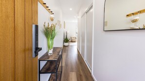 Un pasillo con una puerta de madera, una mesa con un jarrón, una planta y un espejo en la pared.