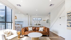 Una sala de estar moderna con un sofá de cuero, una mesa de centro redonda y una cocina al fondo.
