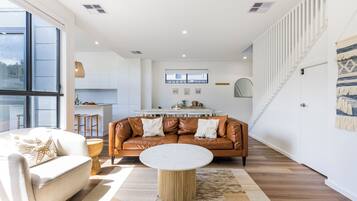 A modern living room with a leather sofa, a round coffee table, and a kitchen in the background.