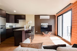 A modern kitchen with dark cabinets, a central island, and a flat-screen TV on a wooden stand. - ¡A pasos de Barrio Antiguo! Cama King + Parking (Monterrey)